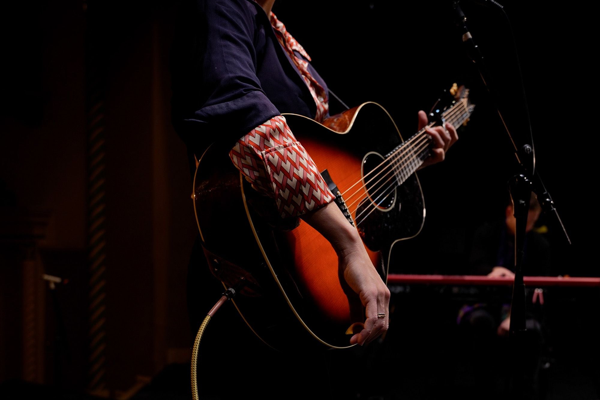 Close-up of May Erlewine playing a sunburst acoustic guitar on a darkened stage at Wealthy Theatre